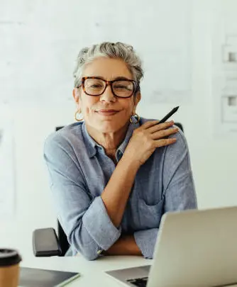 Mujer de 40 años sonriente sentada en su oficina frente a una laptop, satisfecha por tener una estrategia de retiro con la ley del IMSS de 1997