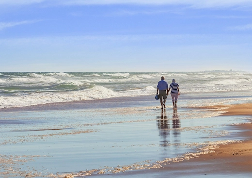 Pareja adulta mayor caminando por la arena hacia el horizonte junto al mar, disfrutando su retiro gracias a la ley del IMSS de 1973